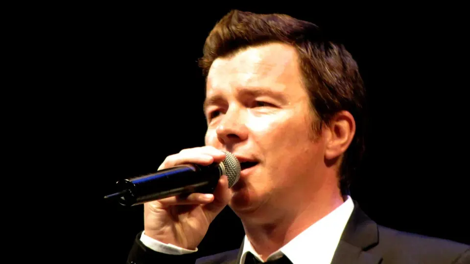 Rick Astley singing into a handheld microphone on stage
